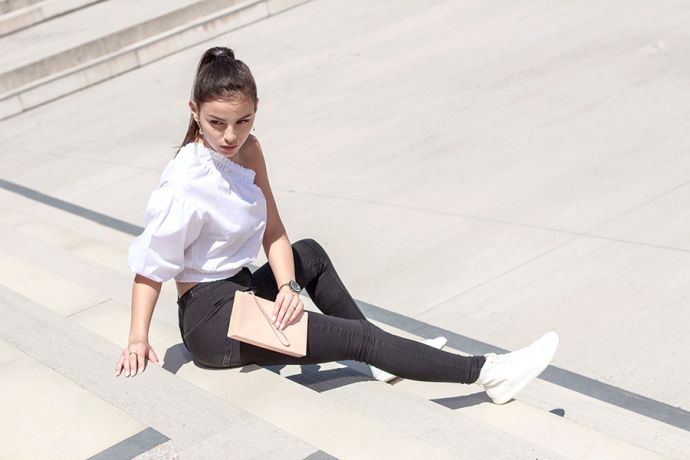 A brown-haired woman in a white top with the body-coloured leather Lux Clutch bag