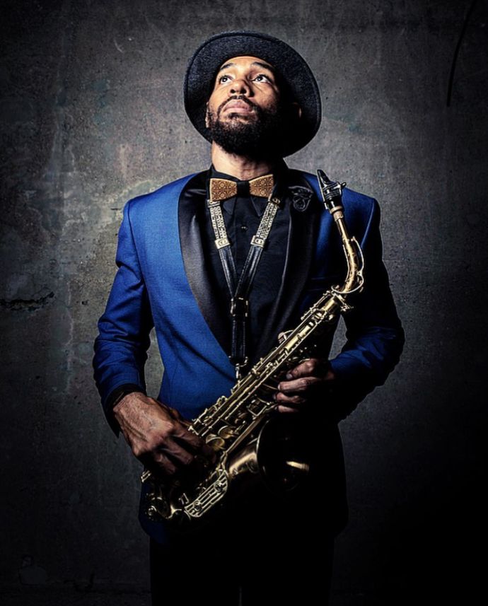 The musician Saxappeal in a blue jacket with a hat and the Bellis wooden bow tie holding a saxophone in his hand