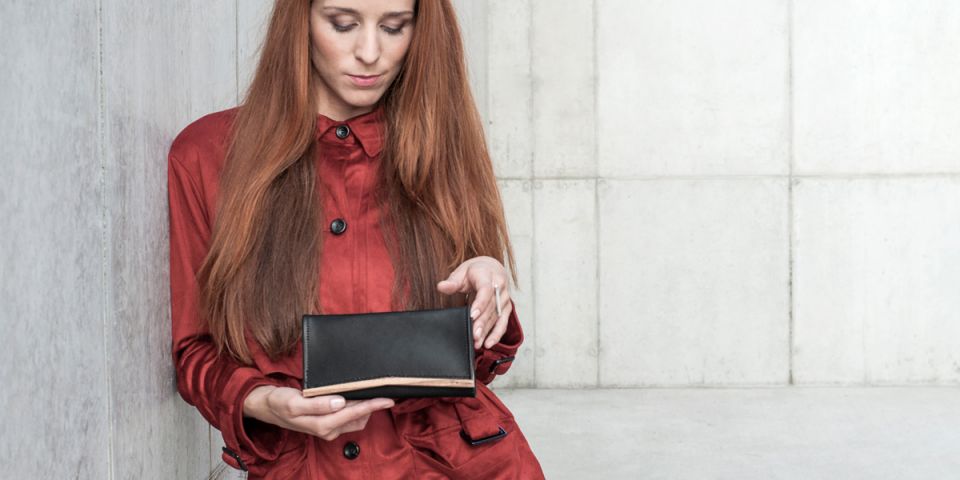 A woman with red hair in an orange coat holding a wallet made of wood and leather Api Woman Wallet