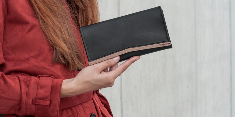 A woman with red hair in an orange coat holding a wallet made of wood and leather Caleo Woman Wallet A woman with red hair in an orange coat holding a wallet made of wood and leather Caleo Woman Wallet