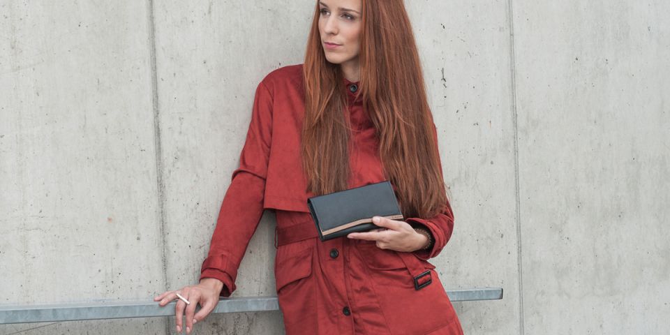 A woman with red hair in an orange coat holding a wallet made of wood and leather Caleo Woman Wallet