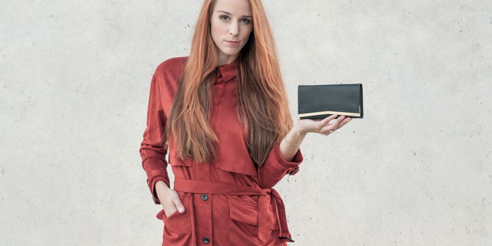 A woman with red hair in an orange coat holding a wallet made of wood and leather Liti Woman Wallet A woman with red hair in an orange coat holding a wallet made of wood and leather Liti Woman Wallet