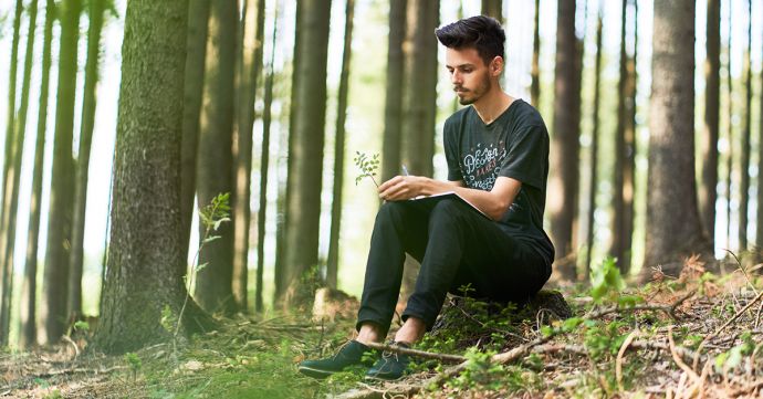 A man sits in a forest and writes in his BeWooden notebook