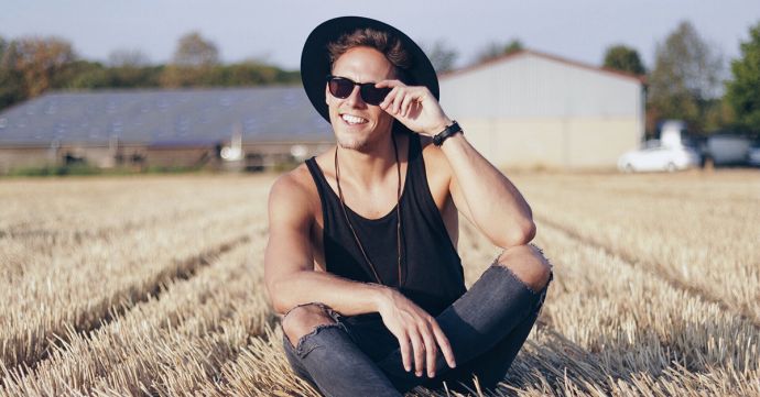 A man is sitting in a field with the black Nox hat